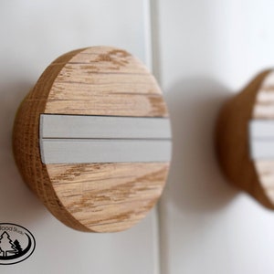 Op de afbeelding: Twee ronde houten knoppen met een zilveren metalen band in het midden. De knoppen hebben een houtnerfpatroon en zijn lichtbruin.