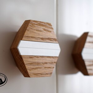 Könnte beinhalten: Zwei sechseckige Holzknauf für Schränke mit einem weißen Streifen in der Mitte. Die Knäufe sind aus hellbraunem Holz mit natürlicher Maserung.