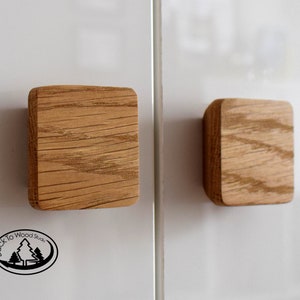 May include: Two square wooden cabinet pulls with rounded edges. The pulls are made of light brown wood and have a visible wood grain pattern. The pulls are mounted on a white surface. The logo "Back to Wood Studio" is visible.