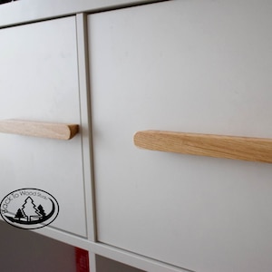 Pu&ograve; includere: Due maniglie per armadio in legno con bordi arrotondati, montate su ante di armadio bianche. Le maniglie sono in legno chiaro e sono lunghe circa 30 cm.