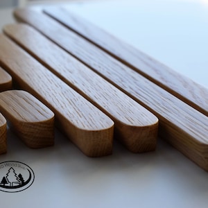Pu&ograve; includere: Un set di sette maniglie per armadi in legno di diverse dimensioni, tutte con una forma arrotondata leggermente curva. Le maniglie sono in legno marrone chiaro con una venatura naturale. Le maniglie sono disposte a scalare, con la maniglia pi&ugrave; grande in alto e la pi&ugrave; piccola in basso. Tutte le maniglie sono realizzate da Back to Wood Studio.