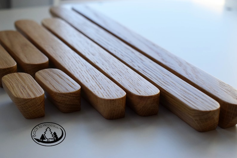 Pu&ograve; includere: Un set di sette maniglie per armadi in legno di diverse dimensioni, tutte con una forma arrotondata leggermente curva. Le maniglie sono in legno marrone chiaro con una venatura naturale. Le maniglie sono disposte a scalare, con la maniglia pi&ugrave; grande in alto e la pi&ugrave; piccola in basso. Tutte le maniglie sono realizzate da Back to Wood Studio.