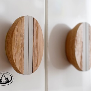 May include: Two round wooden knobs with a vertical gray stripe down the center. The knobs are mounted on a white surface.