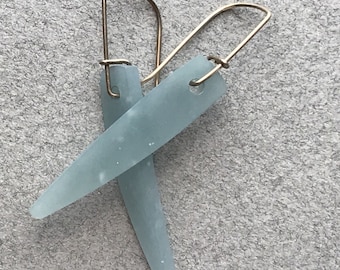 May include: A pair of light blue glass earrings with gold wire hooks. The earrings are long and narrow, with a slightly pointed end.