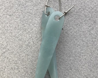 May include: A pair of long, slender, pale seafoam green earrings with a matte, frosted finish. Each earring features a tapered, flat shape with a circular hole at the top, suspended from a simple silver-toned metal wire hook closure.
