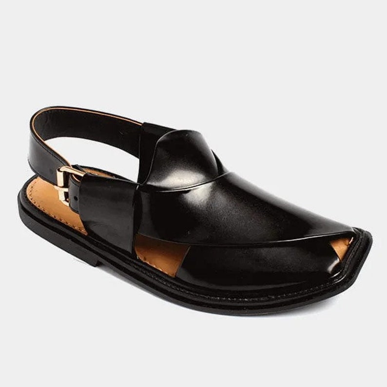 May include: Black leather sandal with a closed toe design and a strap around the ankle. The sandal features a gold-colored buckle and a contrasting tan insole. The shoe has a sleek, modern appearance.