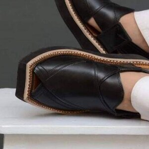 May include: Black leather sandals with a thick sole. The sandals have a stitched design and a light brown trim around the sole. The image shows the sandals on a white surface.