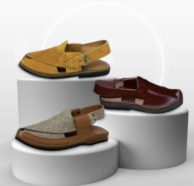 May include: Three pairs of open-toe sandals in different colors: tan suede, brown leather, and a tan and brown fabric combination. Each sandal has a strap around the ankle and a flat sole. The sandals are displayed on white pedestals.