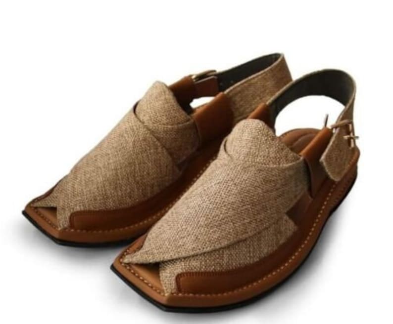 May include: A pair of brown and tan sandals with a woven fabric upper and leather accents. The sandals have a strap around the ankle and a buckle closure. The soles are brown and the overall design is casual and comfortable.
