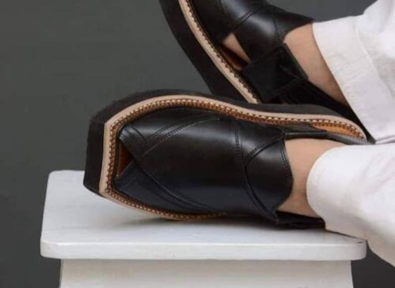 May include: Black leather sandals with a thick sole. The sandals have a stitched design and a light brown trim around the sole. The image shows the sandals on a white surface.