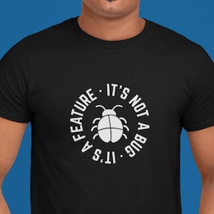 May include: A black t-shirt with a white graphic of a bug and the text "It's a feature. It's not a bug."
