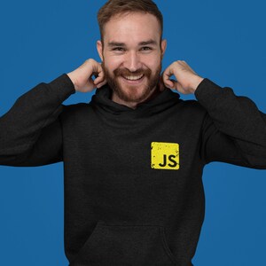 May include: A black hoodie with a yellow square patch that says "JS" on it. The person wearing the hoodie is smiling.