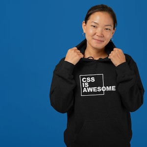May include: A black hoodie with a white square on the front that says "CSS IS AWESOME". A person is wearing the hoodie and smiling at the camera.