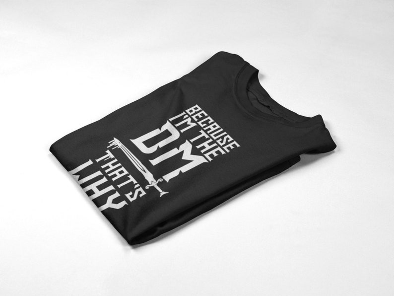 Puede incluir: Camiseta negra con texto blanco que dice "Because I'm the DM That's why". Se incluye un gr&aacute;fico de espada en el texto.