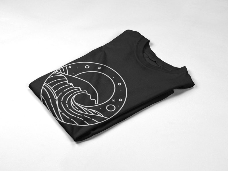 K&ouml;nnte beinhalten: Ein schwarzes T-Shirt mit einem wei&szlig;en Grafikdruck einer Welle in einem Kreis mit Sternen und Monden.