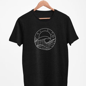 K&ouml;nnte beinhalten: Ein schwarzes T-Shirt mit einer wei&szlig;en Linienzeichnung einer Welle, eines Mondes und Sternen in einem Kreis.