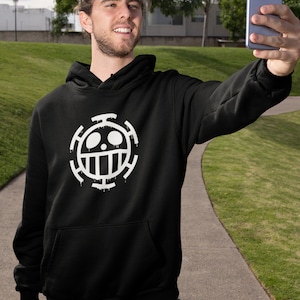 May include: A black hoodie with a white graphic of the "One Piece" anime character, Trafalgar D. Water Law's, symbol. The symbol is a skull with a crossbones and a circle around it.