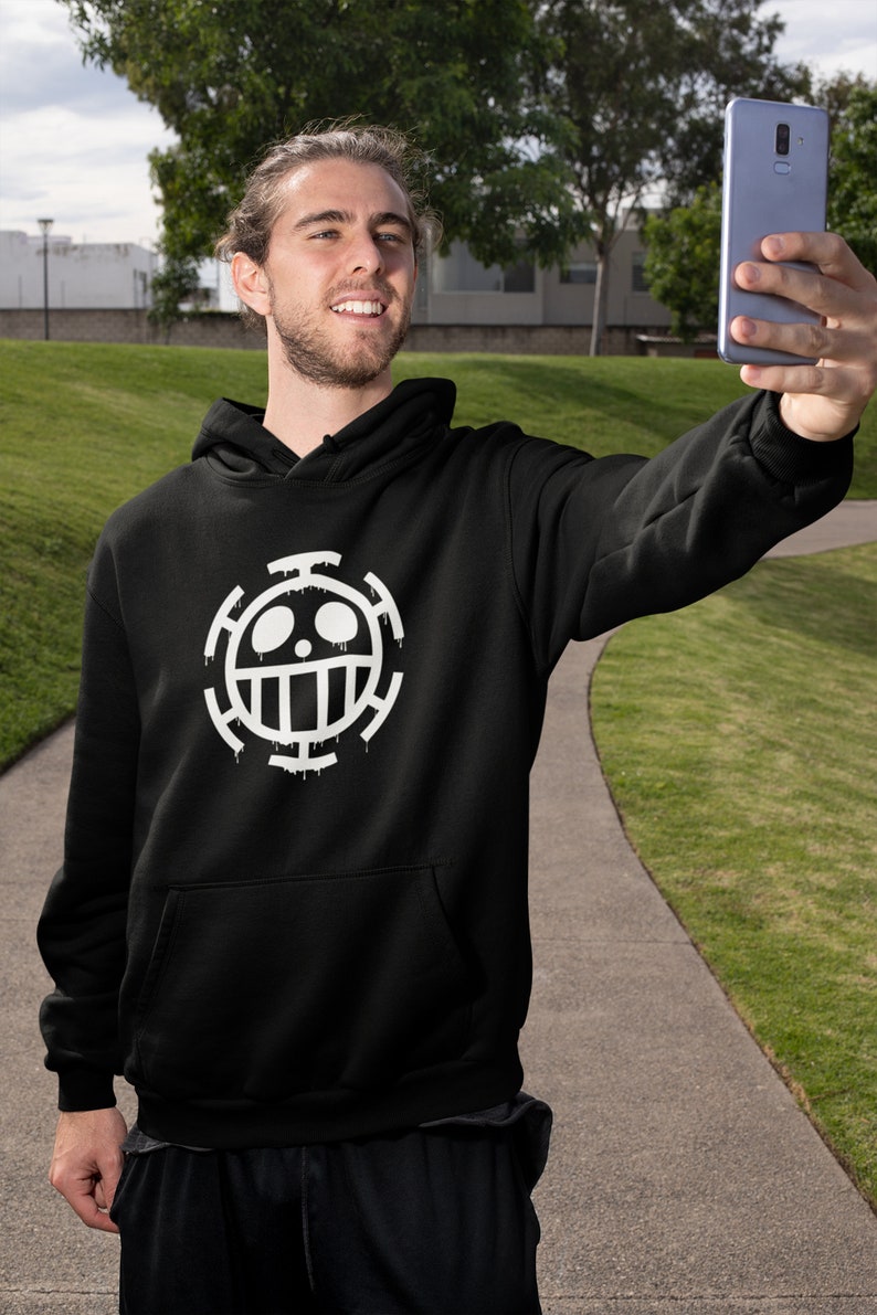 May include: A black hoodie with a white graphic of the "One Piece" anime character, Trafalgar D. Water Law's, symbol. The symbol is a skull with a crossbones and a circle around it.