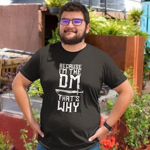 Puede incluir: Camiseta negra con texto blanco que dice "Because I'm the DM That's Why". Un gr&aacute;fico de espada est&aacute; sobre la palabra "DM".