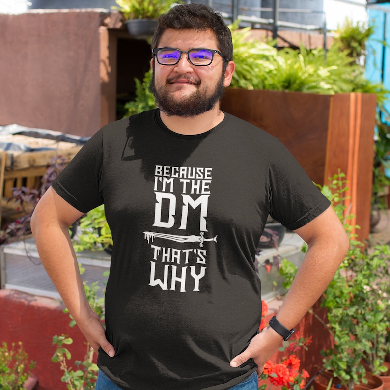 Puede incluir: Camiseta negra con texto blanco que dice "Because I'm the DM That's Why". Un gr&aacute;fico de espada est&aacute; sobre la palabra "DM".