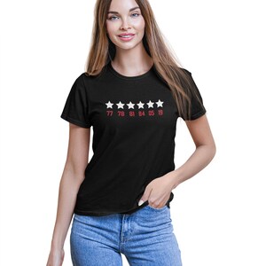 Pu&ograve; includere: Maglietta nera con cinque stelle bianche e i numeri 77 78 81 84 05 19 stampati in rosso sotto.