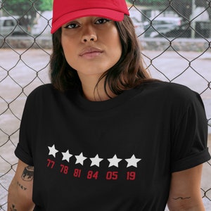 Pu&ograve; includere: Maglietta nera con una valutazione a cinque stelle bianche e i numeri 77 78 81 84 05 19 stampati sotto le stelle.