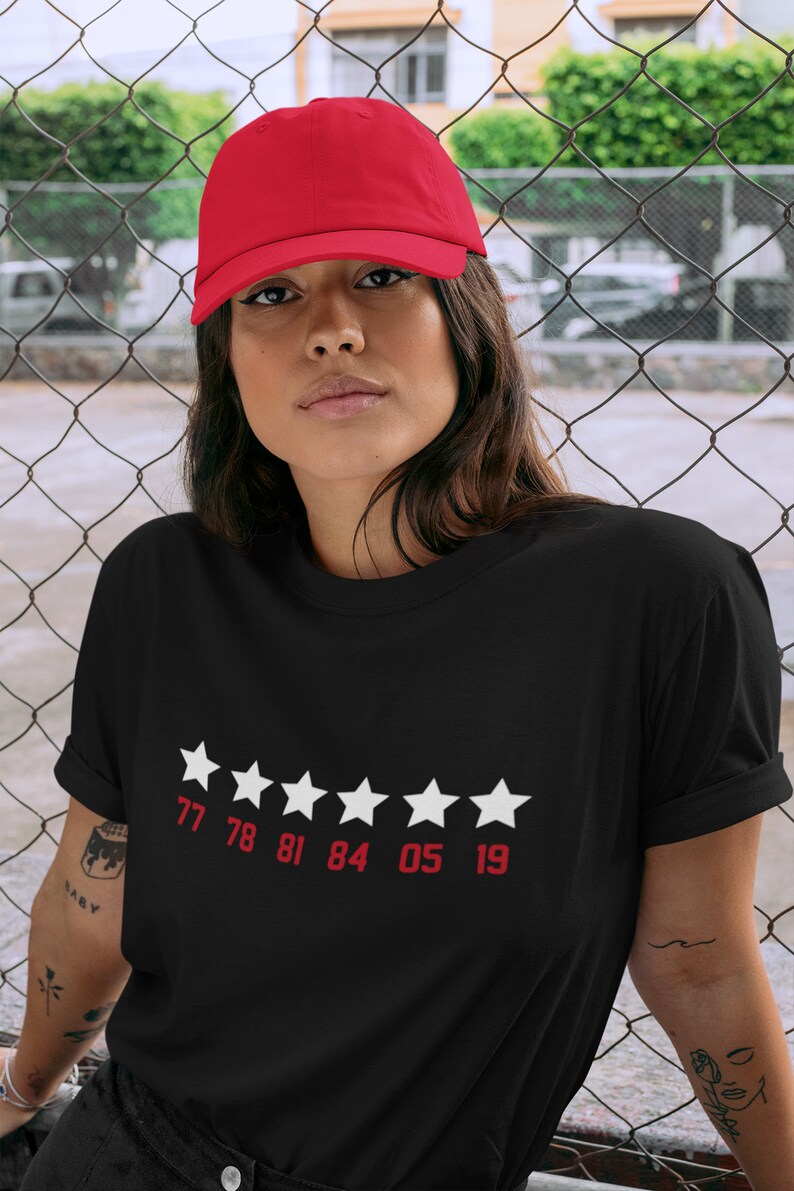 Pu&ograve; includere: Maglietta nera con una valutazione a cinque stelle bianche e i numeri 77 78 81 84 05 19 stampati sotto le stelle.