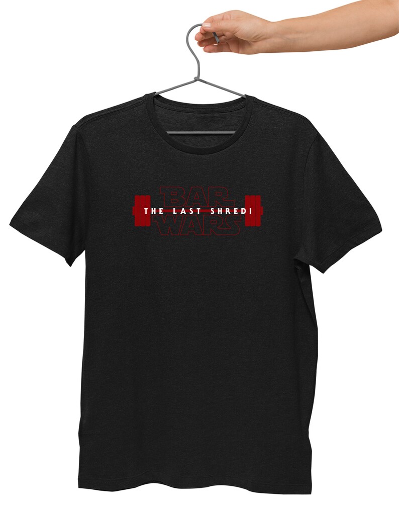 May include: Dark grey t-shirt featuring the red text "BAR WARS THE LAST SHREDI" and red barbell graphics. The t-shirt is suspended from a metal hanger.