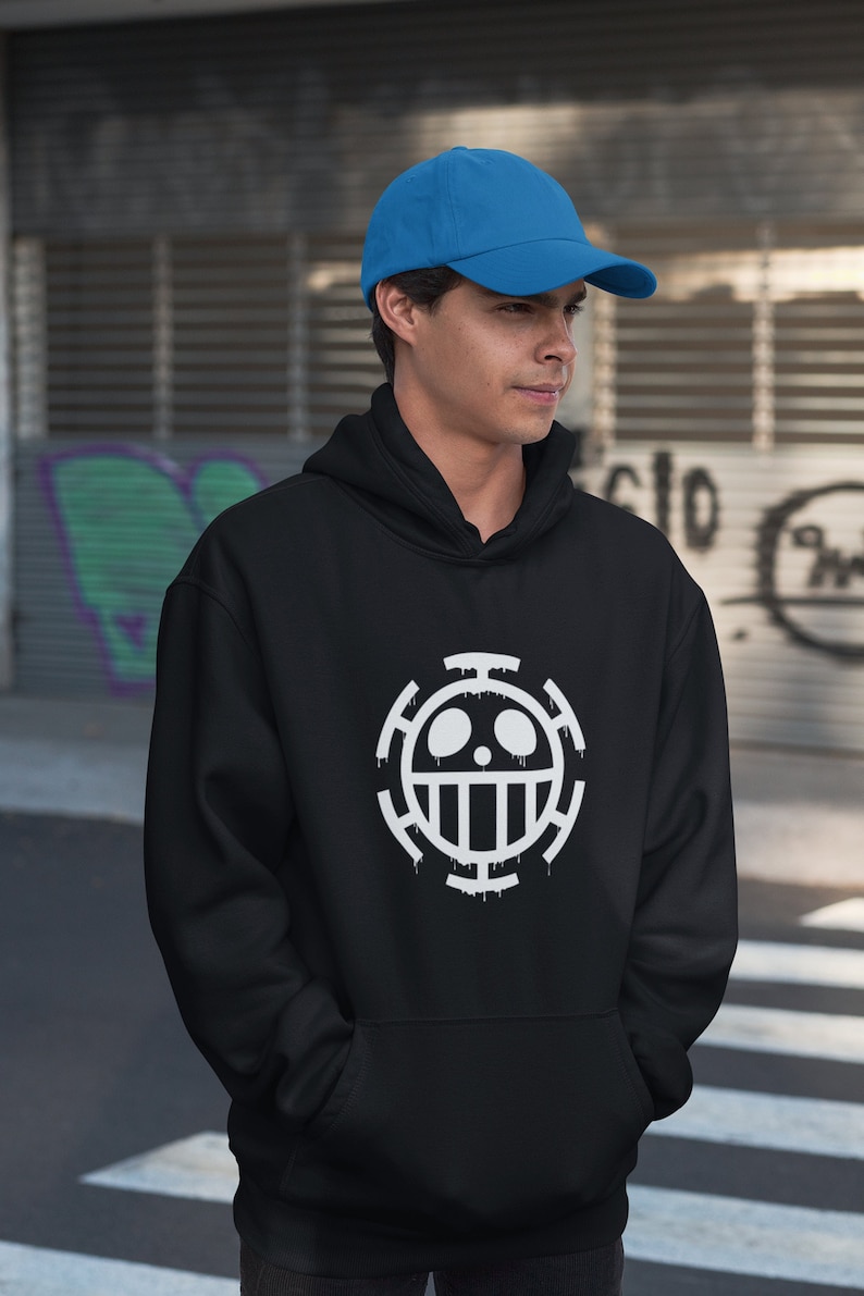 May include: A black hoodie with a white skull and crossbones graphic. The graphic is a stylized version of the Jolly Roger, a pirate flag. The hoodie has a drawstring hood and a kangaroo pocket. The model is wearing a blue baseball cap.