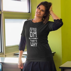 Puede incluir: Una camiseta negra con texto blanco que dice "Because I'm the DM That's Why" con un gr&aacute;fico de espada.
