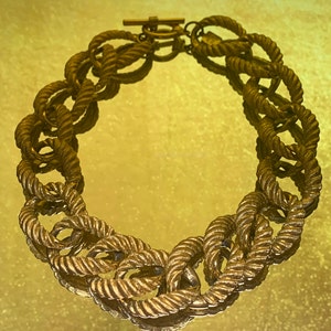 May include: A gold-toned chain necklace with a rope-like design. The necklace is made of linked oval shapes, each with a twisted rope design.
