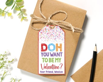 Può includere: Un'etichetta regalo colorata per San Valentino con coriandoli e il testo "DOH YOU WANT TO BE MY VALENTINE? Your Friend, Weston".