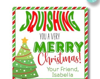 May include: A white card with red and green stripes around the border. The card has a green and red cartoon tree with a yellow star on top. The text on the card reads "Squishing you a very Merry Christmas! Your Friend, Isabella."