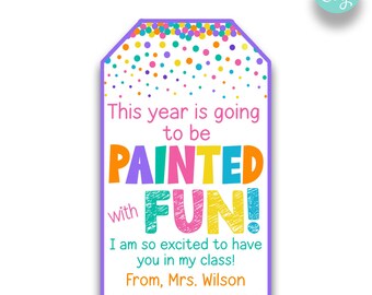 May include: A purple and white tag with colorful confetti and paintbrushes. The text reads "This year is going to be PAINTED with FUN! I am so excited to have you in my class! From, Mrs. Wilson"
