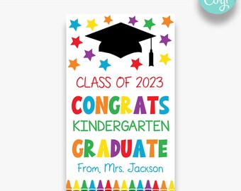 May include: A printable graduation sign with a black graduation cap, colorful stars, and the text "Class of 2023 Congrats Kindergarten Graduate From, Mrs. Jackson". The sign features a row of colorful crayons at the bottom.
