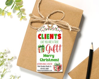 May include: A white gift tag with a red and green Christmas theme. It says "Clients like you are a true gift! Merry Christmas!" and includes a realtor's contact information.