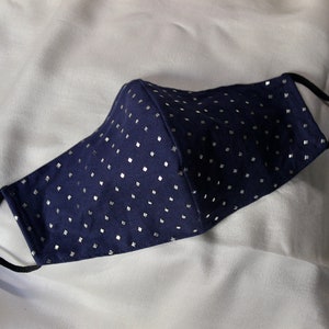 May include: A navy blue face mask with a silver polka dot pattern. The mask has elastic ear loops.