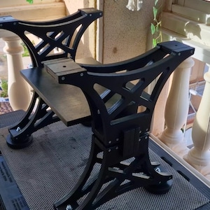 Könnte beinhalten: Schwarze Metall-Tischbeine mit geometrischem Design. Die Beine sind durch eine rechteckige Tischplatte verbunden. Die Tischbeine stehen auf einer dunklen Oberfläche, mit einem Balkon und einem Fenster im Hintergrund.