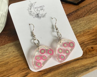 May include: Clear, teardrop-shaped earrings with a dragon fruit design. Each earring features a pink border with black and white dots, and silver-colored ear wires. The earrings are displayed on a white card with the text "POURED By Addy".