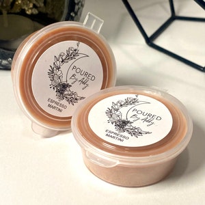 May include: Two small, round, clear plastic containers filled with a light brown substance. Each container has a white label with the text "POURED By Addy" and "Espresso Martini" printed on it, along with a floral design.