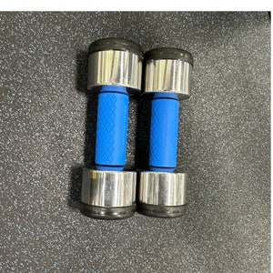 Puede incluir: Un par de mancuernas plateadas con mangos de goma azul. Las mancuernas est&aacute;n sobre una superficie negra texturizada.