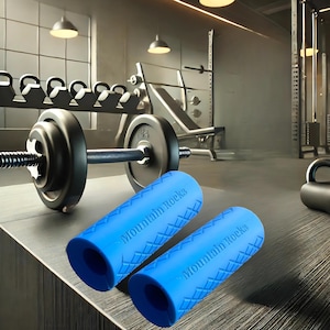 Puede incluir: Dos agarres azules para fortalecer la fuerza de agarre con el texto "Mountain Rocks" impreso en ellos. Los agarres est&aacute;n sobre una superficie de madera delante de una barra.