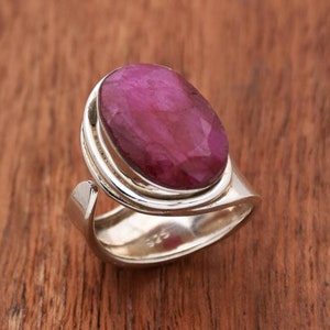 May include: A silver ring with a large, oval-shaped, deep pink gemstone set in a silver bezel. The ring has a simple, modern design.