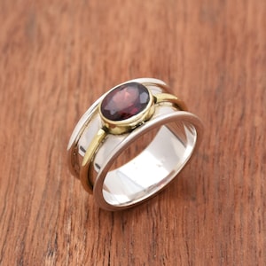 May include: A silver and gold ring with a red gemstone. The ring has a wide band with a gold accent.