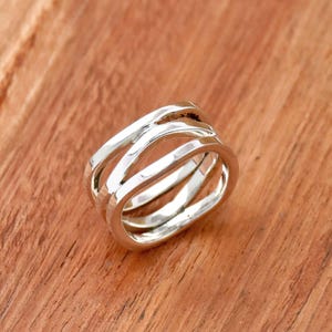 Può includere: Un anello d'argento con tre bande intrecciate. Le bande sono lisce e hanno una texture leggermente martellata.