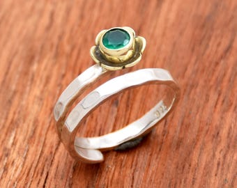 May include: A silver and gold ring with a green gemstone set in a flower design. The ring is twisted and has a hammered finish.