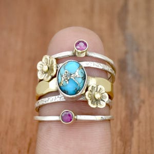May include: A silver and gold ring with a turquoise stone and two small flower accents. The ring is set with two small pink stones.