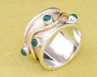 May include: A silver and gold ring with a textured band and three green gemstones. The band is decorated with a wavy gold line.
