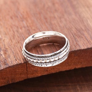 May include: A silver spinning ring with a textured design. The ring is marked with "925" on the inside.