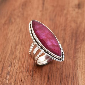 Könnte beinhalten: Ein silberner Ring mit einem großen, ovalen, rosafarbenen Edelstein, der in einem gedrehten Silberband gefasst ist.